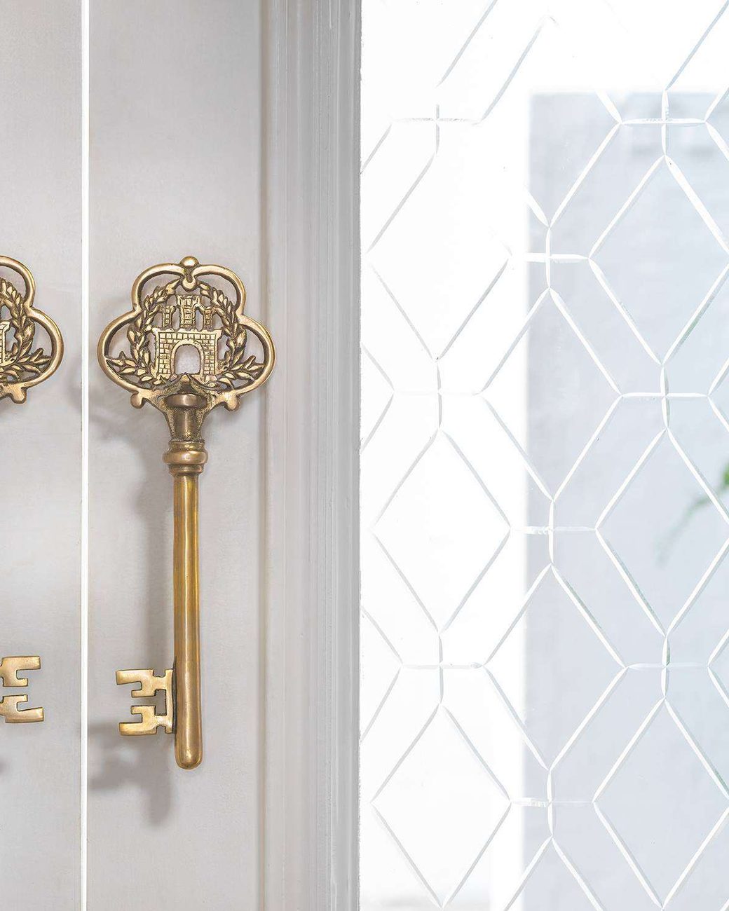 Two ornate gold keys mounted on a white lattice door at Amiraah